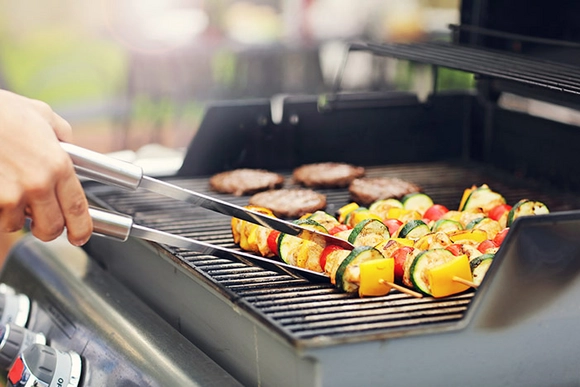 Person grillt Gemüse und Burger mit Grillzange